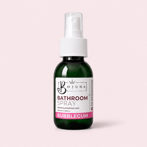 A dark green glass spray bottle of Bojuna Bathroom Spray with a white pump dispenser and a white label featuring pink and black text, set against a solid pale pink background.