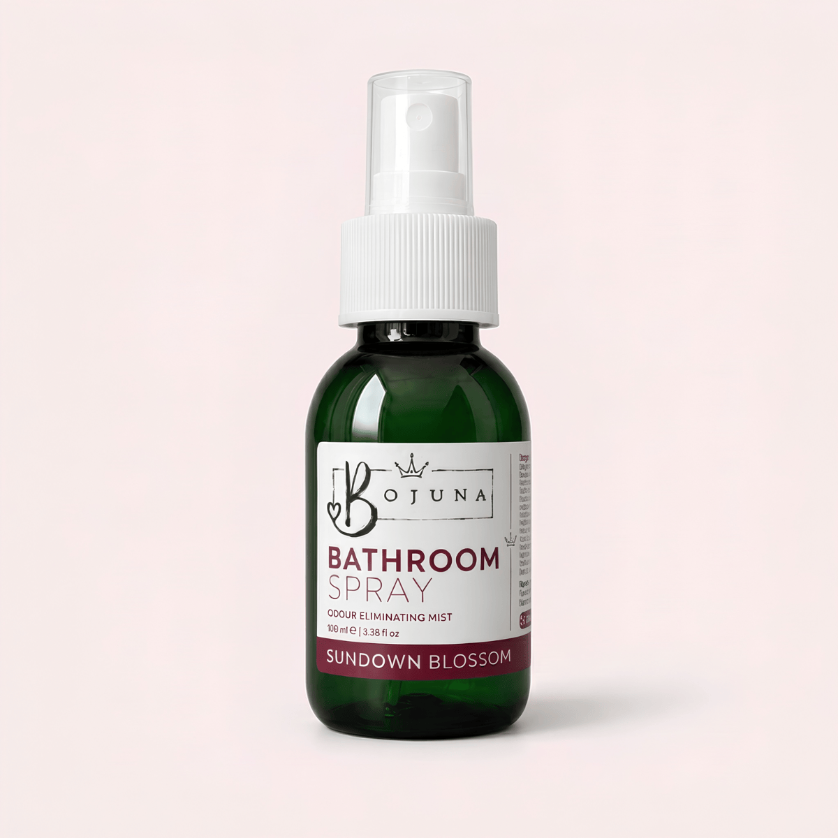 A dark green glass bottle of Botuna Bathroom Spray in Citrus Spice scent, featuring a white spray nozzle and a white label with brown accents, set against a solid pale pink background.