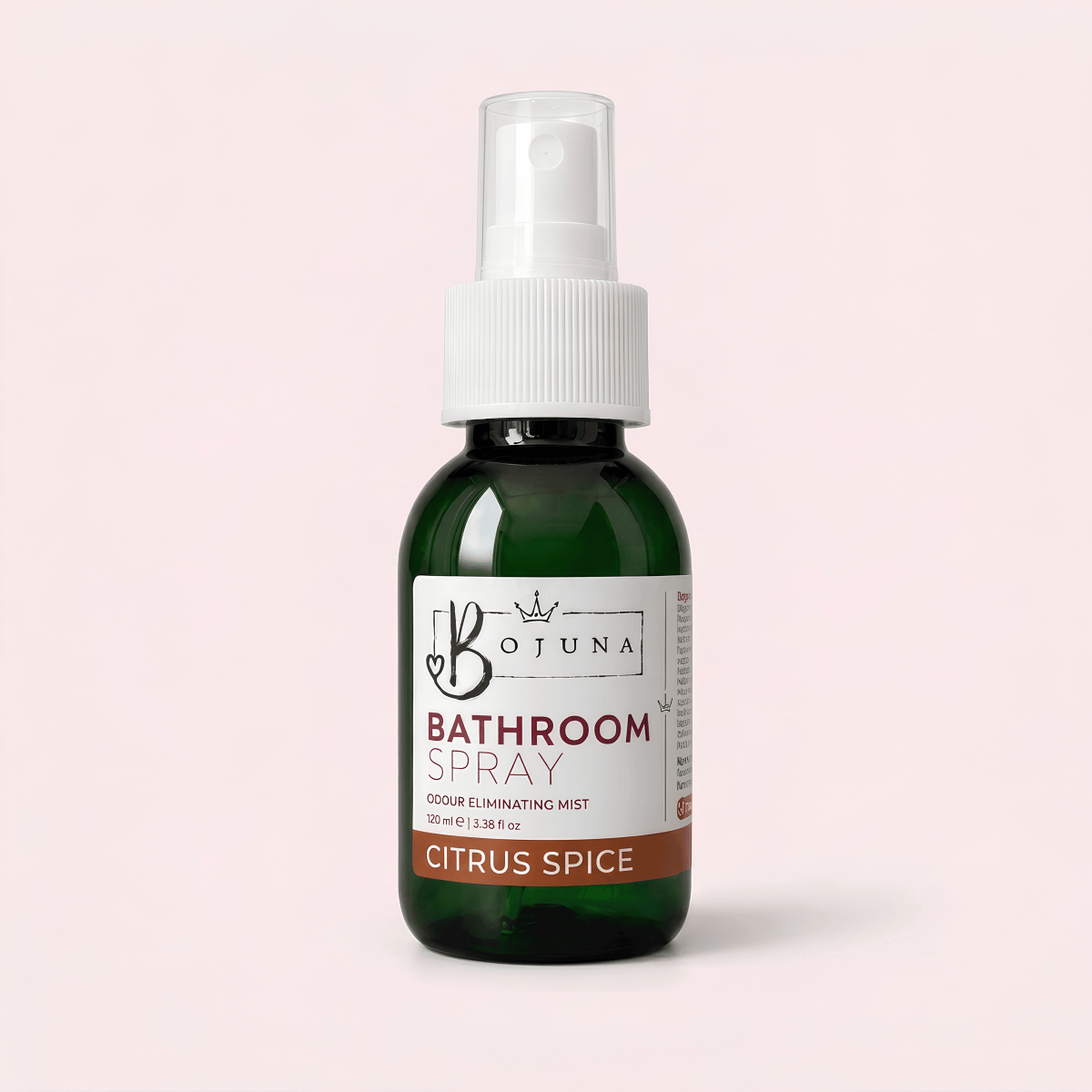 A dark green glass bottle of Botuna Bathroom Spray in Citrus Spice scent, featuring a white spray nozzle and a white label with brown accents, set against a solid pale pink background.