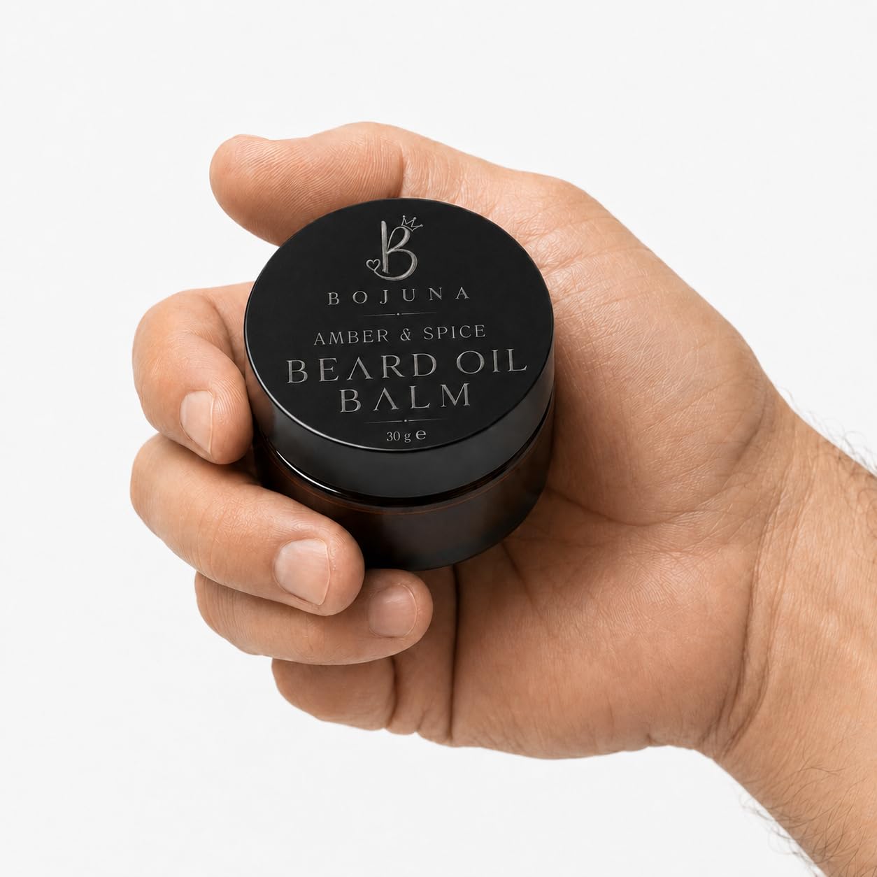 A hand holding a small black round jar of Bojuna Beard Oil Balm against a clean white background.