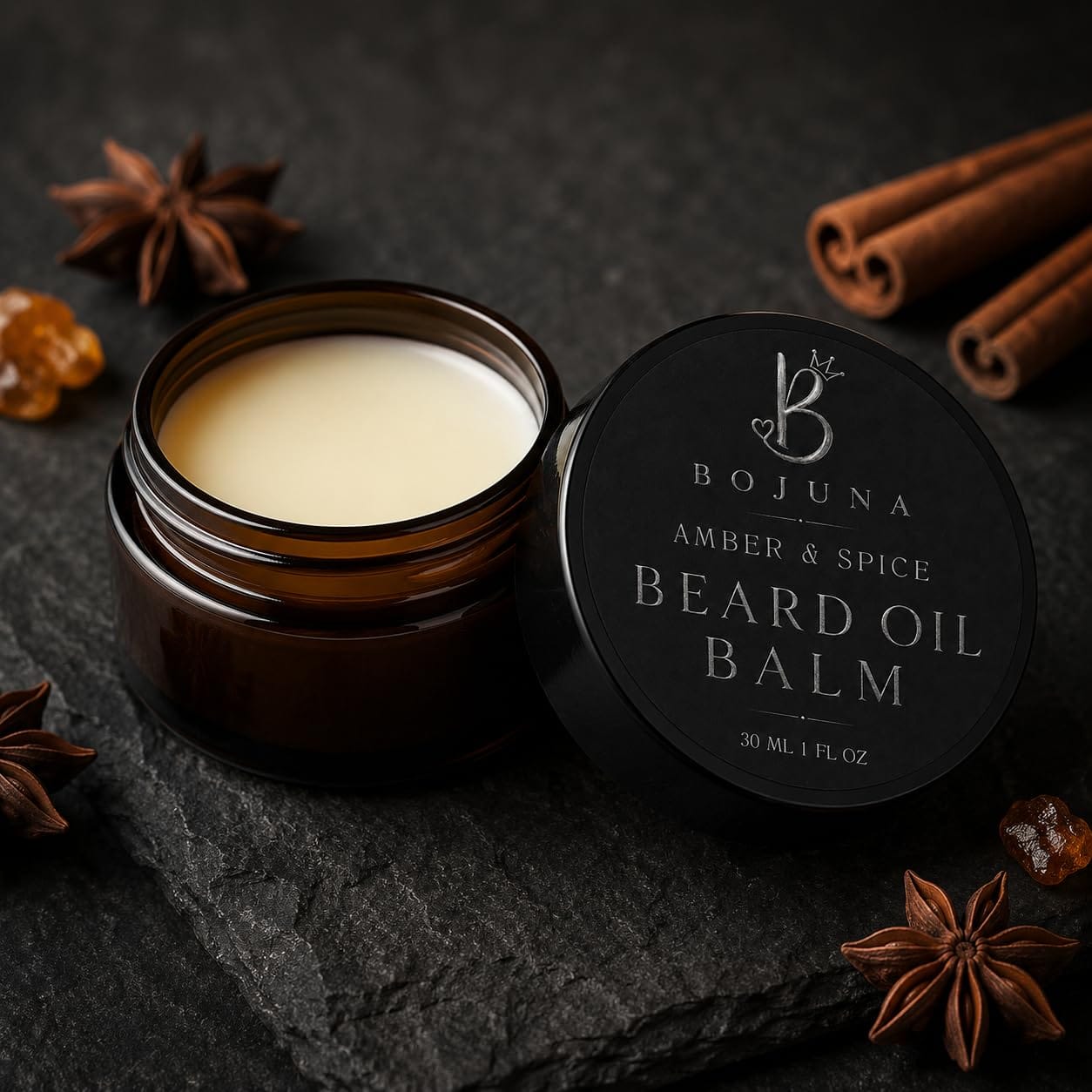 An open amber glass jar of Bojuna Beard Oil Balm with its black lid placed beside it on a dark stone surface, surrounded by star anise and cinnamon sticks.