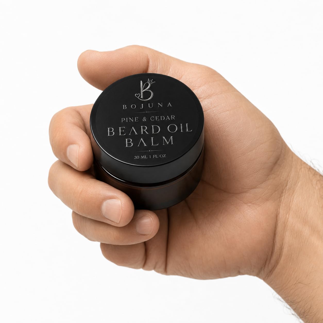 A hand holding a small black round jar of Bojuna Pine & Cedar Beard Oil Balm against a clean white background.
