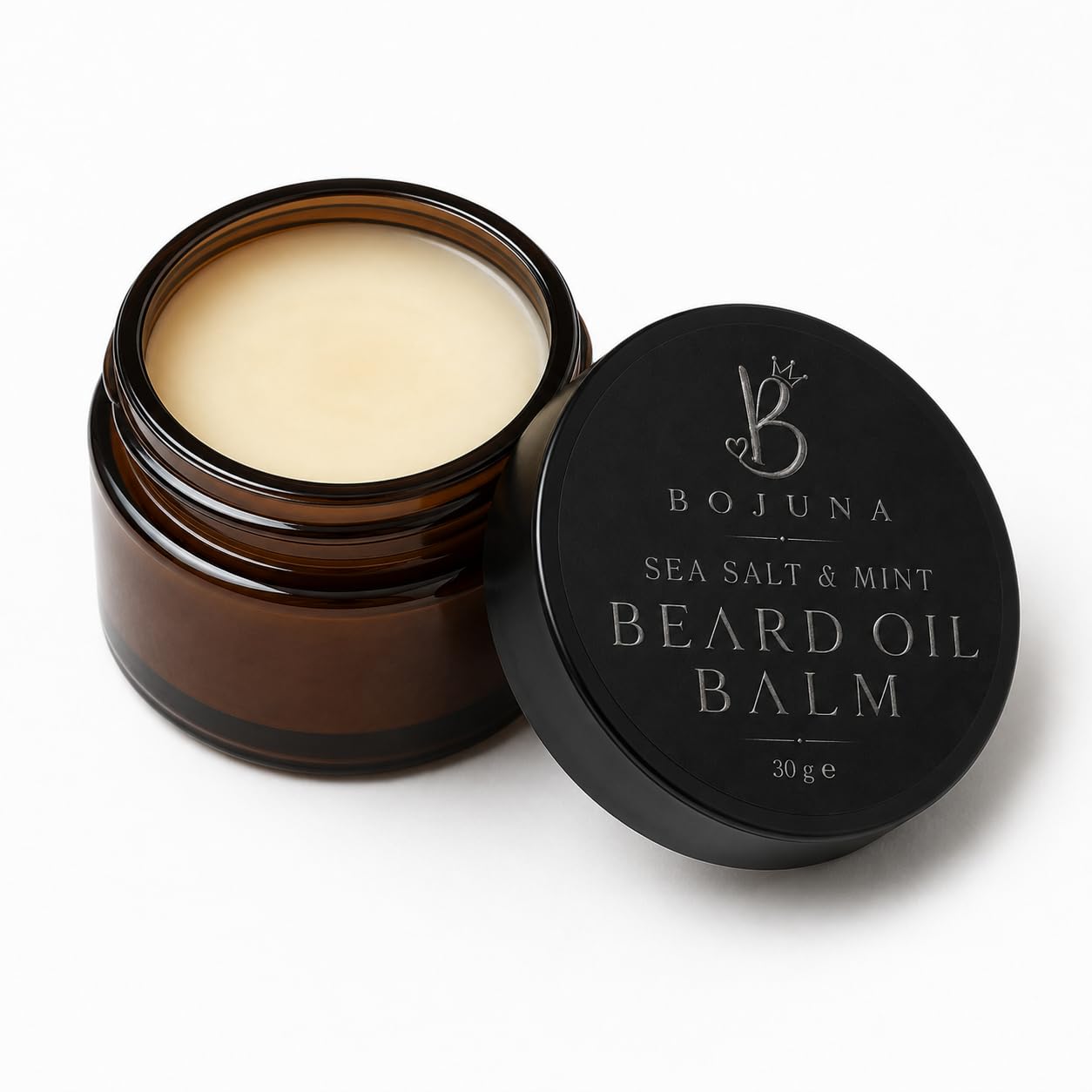 An open amber glass jar of Bojuna Sea Salt & Mint Beard Oil Balm next to its black lid, which features silver text and logo, on a clean white background.