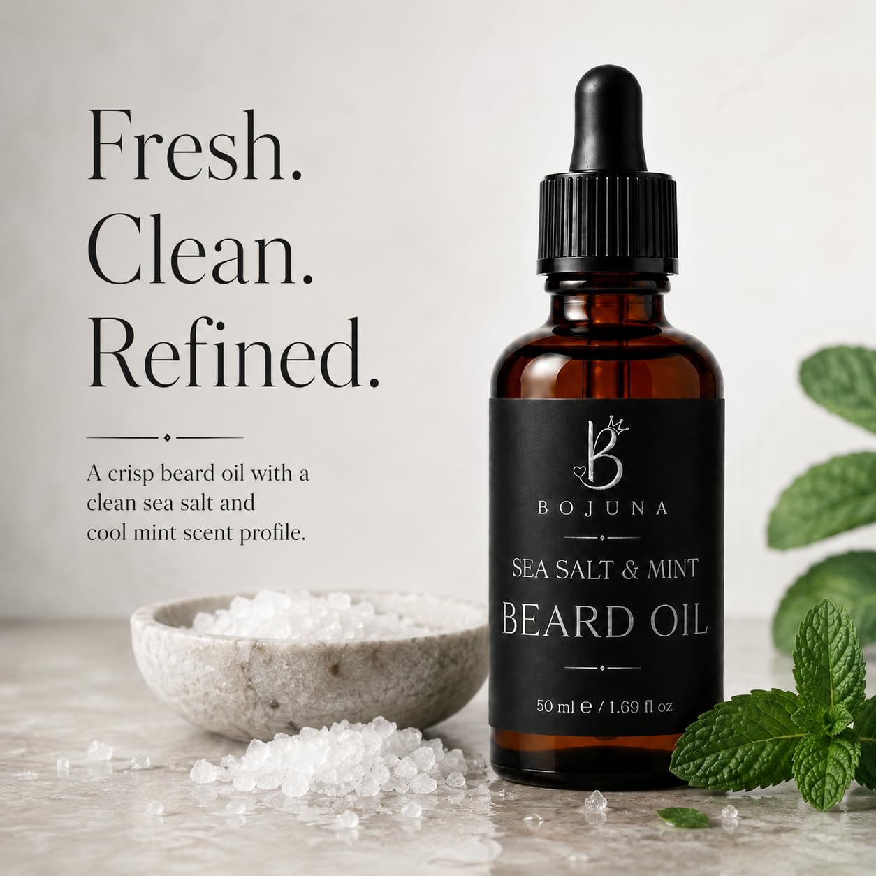 A bottle of Bojuna Sea Salt & Mint Beard Oil stands on a light stone surface beside a small bowl of sea salt and mint leaves, with large marketing text on the left.