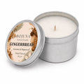 An open silver metal tin candle next to its lid, which features a round label reading 'BOJUNA Scented Candle GINGERBREAD Coconut & Rapeseed Hand Poured 80 g e'. The candle wax inside is a warm off-white/cream color.