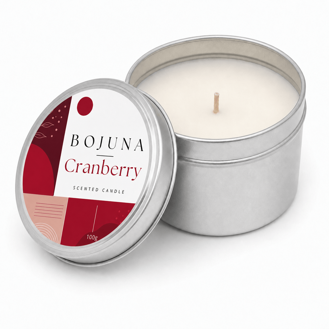 An open silver metal tin candle with white wax and a single wick, next to its lid. The lid features a label for 'BOJUNA Cranberry' scented candle with red and white geometric patterns.
