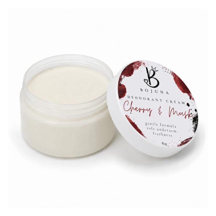 An open clear plastic jar of Bojuna Deodorant Cream next to its white lid, which features a cherry and musk scent label with red and black accents, on a white background.