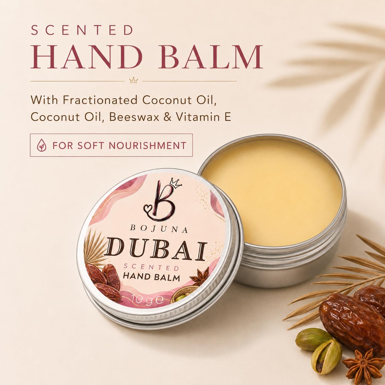 An open round tin of Bojuna Dubai Scented Hand Balm sits beside its labeled lid on a warm cream background, with text describing ingredients and decorative botanical props including dates, pistachios, and star anise.