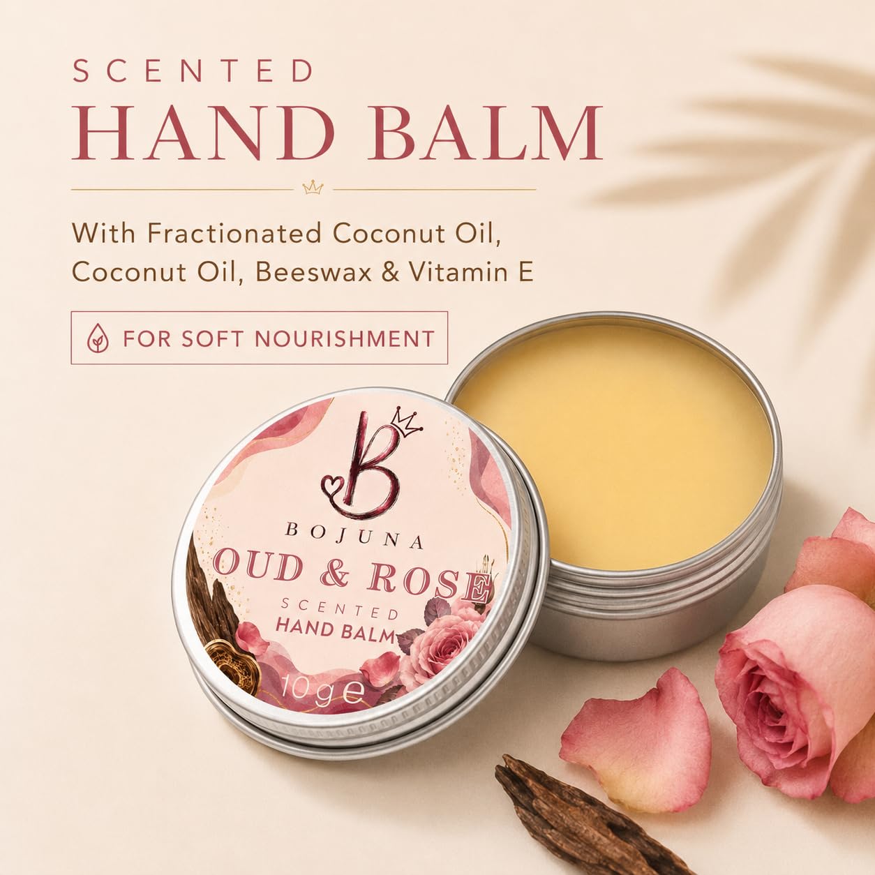 Bojuna Oud & Rose scented hand balm in a round silver tin, shown open with the balm visible next to the labeled lid. The image includes decorative rose petals, a cinnamon stick, and text describing the ingredients on a soft beige background.