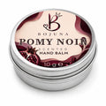 A round silver metal tin of Bojuna Pomy Noir Scented Hand Balm, featuring a cream and dark red label with pomegranate illustrations.