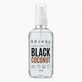 A clear plastic spray bottle of BOJUNA HOME Black Coconut Linen & Fabric Spray, containing a transparent liquid, with a white spray nozzle and a white label featuring black and brown text.
