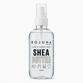 A clear plastic spray bottle of Bojuna Home Shea Butter Linen & Fabric Spray, containing a transparent liquid, with a white spray nozzle and a white label featuring black and beige text.