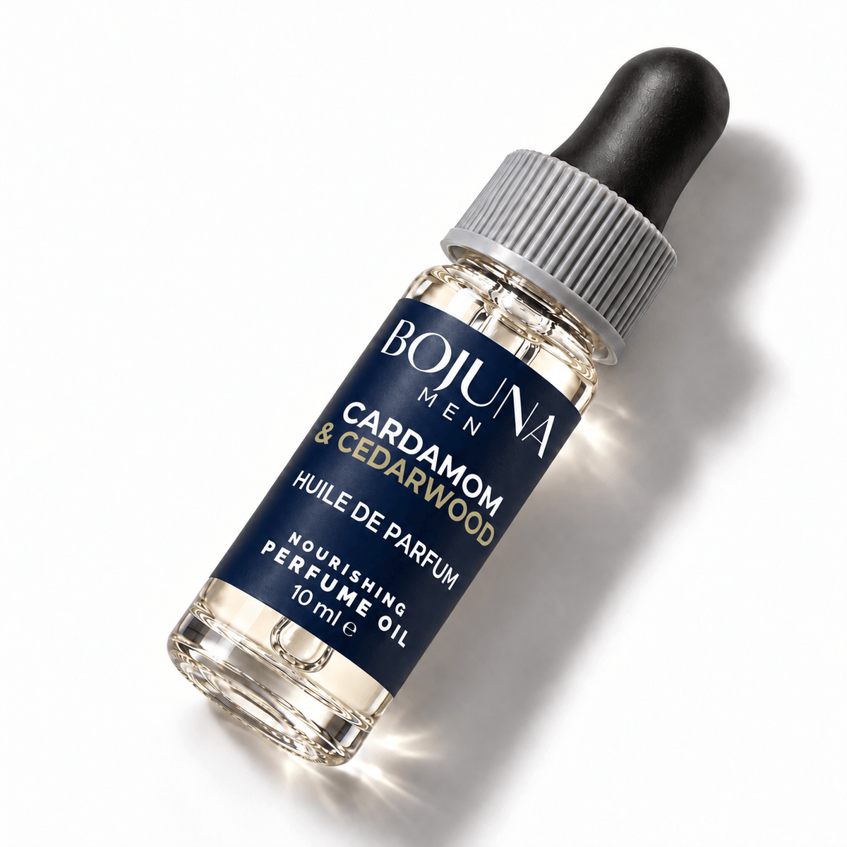Bojuna Men Cardamom & Cedarwood nourishing perfume oil 10 ml, lying diagonally on white with a navy label, white first scent line and grey dropper cap.