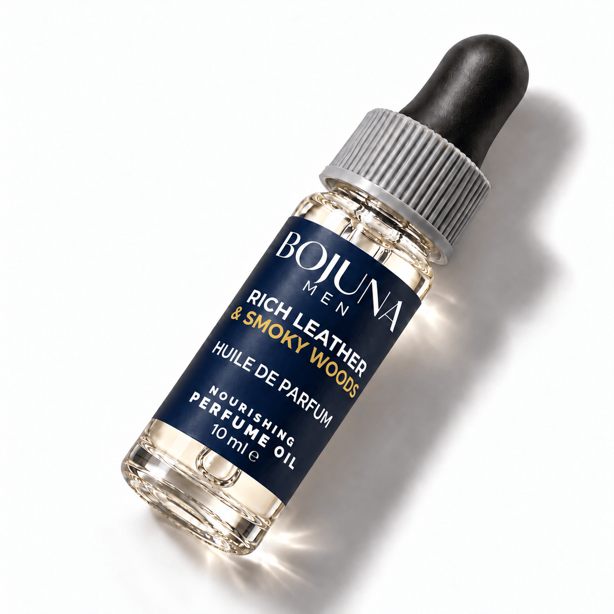 Bojuna Men Rich Leather & Smoky Woods nourishing perfume oil 10 ml, lying diagonally on white with a navy label, white first scent line and grey dropper cap.