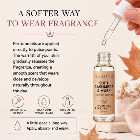 A hand holds a glass dropper above a clear bottle of BOJUNA Soft Cashmere & Musk nourishing perfume oil. The image features a warm beige background with text explaining how to wear fragrance, decorated with autumn leaves and a pink rose.